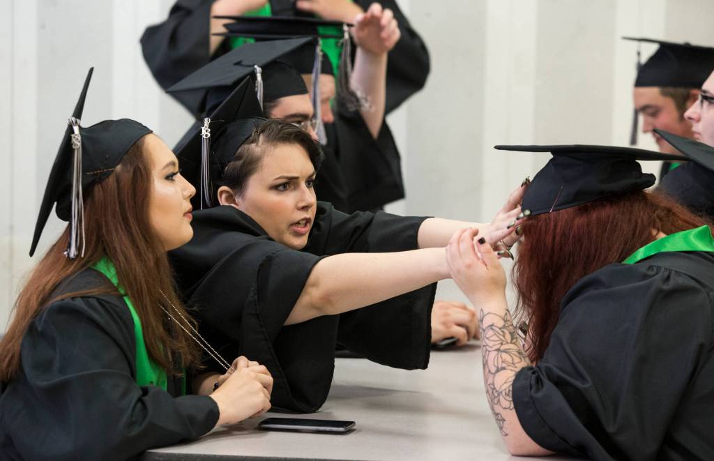 Rhonda Polly reaches out to adjust another students mortarboard before the Sequoia High School graduation ceremony at the Everett Civic Auditorium on Thursday. (Andy Bronson / The Herald)