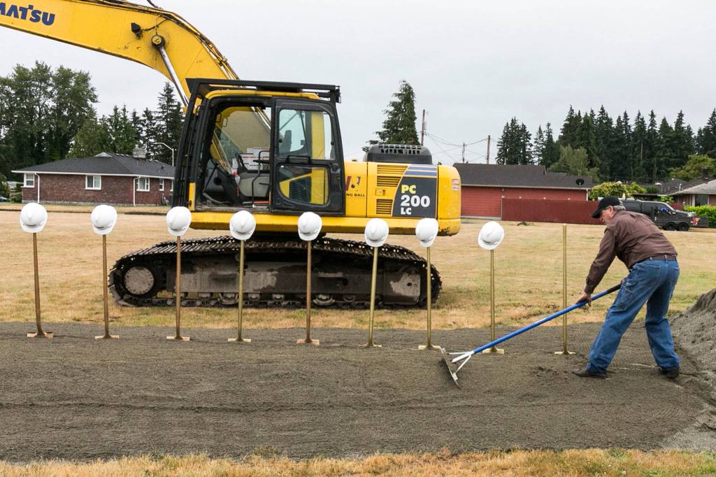 Tom Browne racks the sand to preparation for the ground breaking ceremony at the site of the new YMCA in Everett on June 9. (Kevin Clark / The Herald)