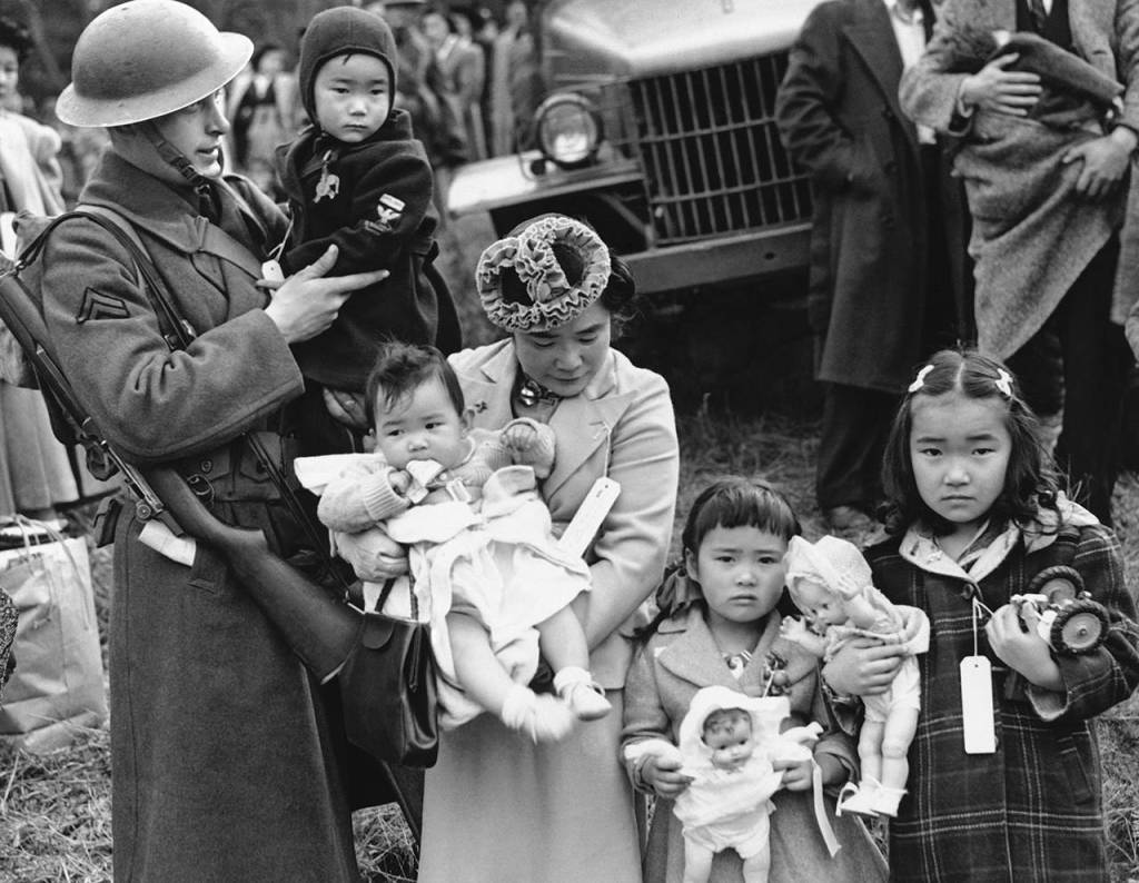 In this 1942 photo, Cpl. George Bushy (left), a member of the military guard which supervised the departure of 237 Japanese people for California, holds the youngest child of Shigeho Kitamoto (center) as she and her children are evacuated from Bainbridge Island. (AP Photo/File)