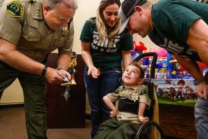 From his wheel chair, Isaiah Kobernik, 4, looks up happily as his parents, Gerad and Anastassia Kobernik and Snohomish County Sheriff Ty Trenary lean over him after his dad pinned a shiny new Sheriff badge on his shirt following a presentation to him by Sheriff Trenary at the Snohomish County Courthouse, Tuesday. Isaiah has Spinal Muscular Atrophy, which affects the motor nerve cells in the spinal chord. (Dan Bates / The Herald)