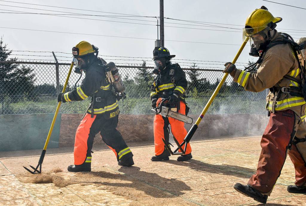 Chau Nguyen (left) tests the integrity of a plywood roof in a May 3 drill meant to mimic a fire in a big box store. (Caleb Hutton / The Herald)