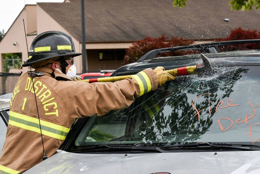 Glass flies as a recruit uses an ax to cut into a windshield at Snohomish Countys first fire academy on June 12. (Caleb Hutton / The Herald)