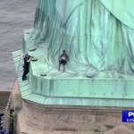In this image a person (center) leans against the robes of the Statue of Liberty on Liberty Island, as one of the police officers climbed up on a ladder to stand on a ledge nearby talking the climber into descending in New York on Wednesday. (PIX11 via AP)