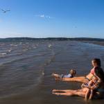 Milissa Simons (right) holds Jet Juliann, 3, while Ashley Elledge (center) watches Lincoln Ballard, 3, swim in the water off of Jetty Island on Thursday in Everett. (Olivia Vanni / The Herald)