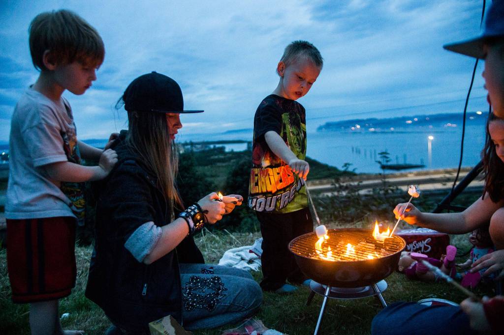 Junior Holmes (right) roasts a marshmallow while Sirus True (left), 5, watches Alyssia Hosmer, 14, light paper for the grill at Legion Memorial Park on Wednesday in Everett. (Olivia Vanni / The Herald)