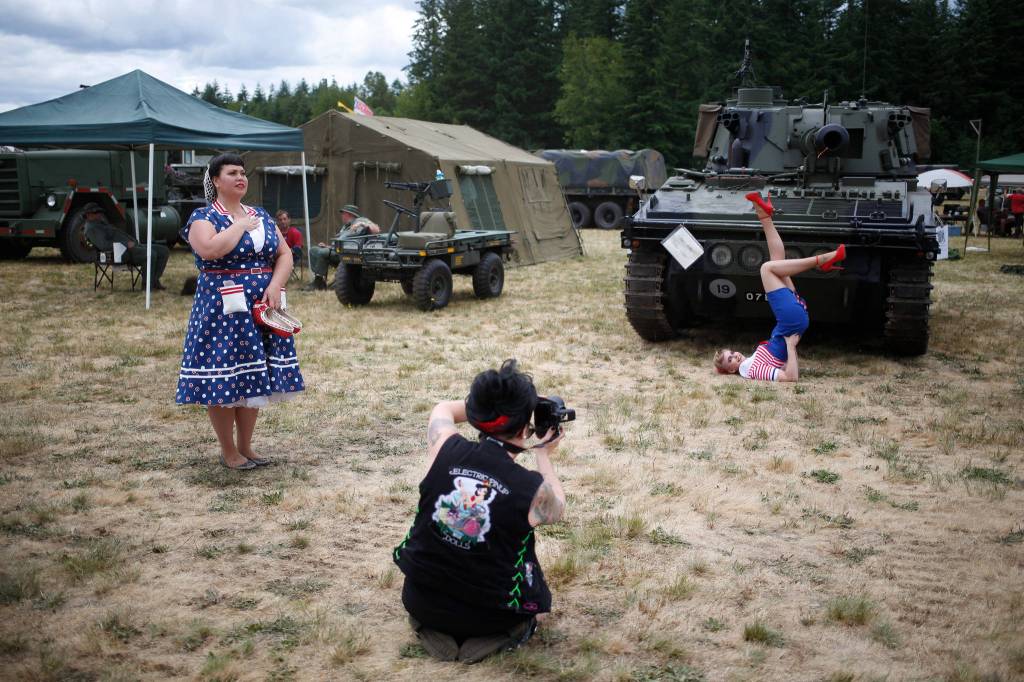 Unaware the National Anthem has started, Brenda Cavoretto photographs Ashley Mckinney posing in a 1940s outfit while Jessica Van Wyk stands at attention at the 50th annual Arlington Fly-In at the Arlington Airport on Saturday. (Andy Bronson / The Herald)