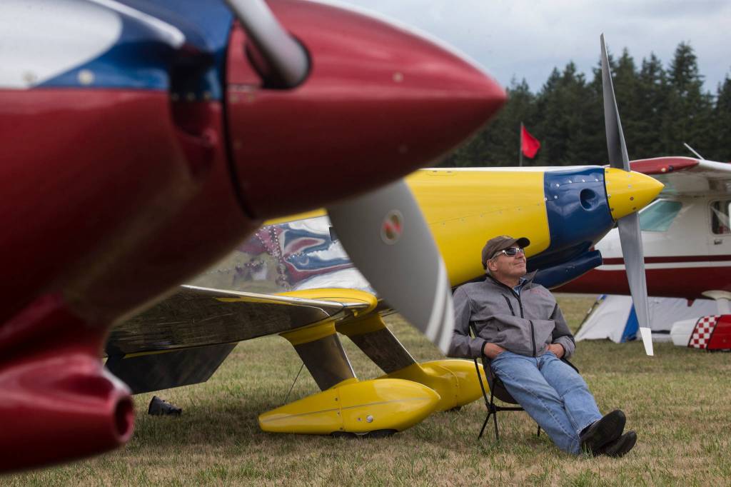 Jay Burrows watches aerobatics as he sits by his Mustang II experimental plane at the 50th annual Arlington Fly-In at the Arlington Airport on Saturday. (Andy Bronson / The Herald)