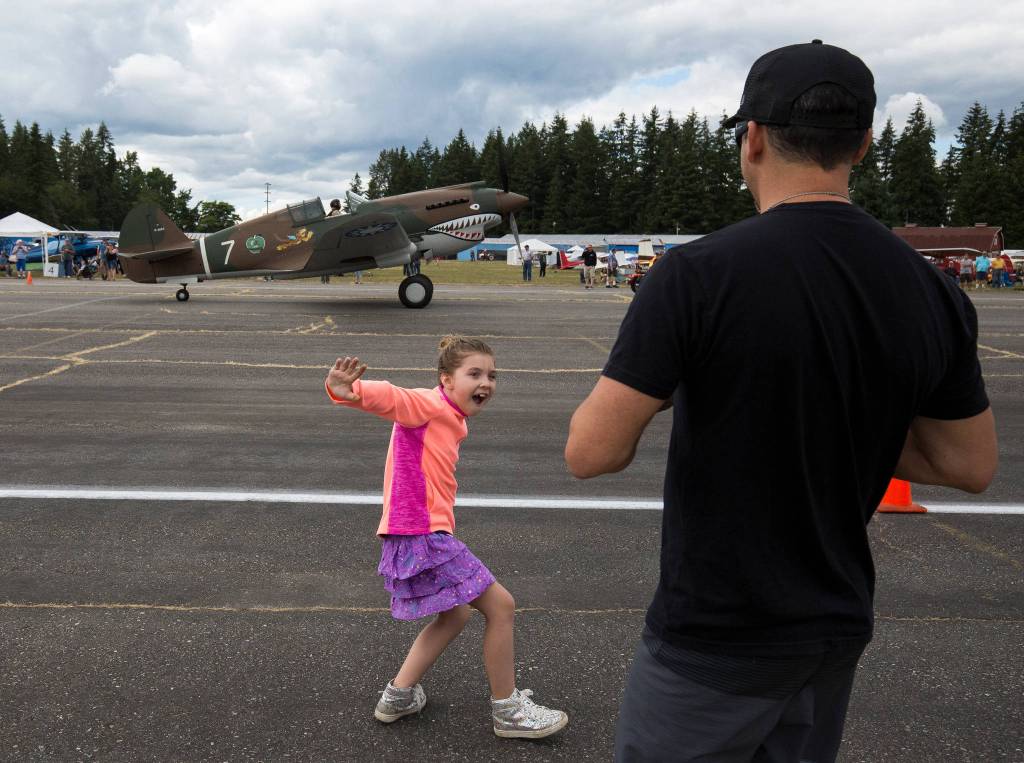 A young girl pretends to be flying as a P-40 Tomahawk plane taxies by during the 50th Annual Arlington Fly-In at the Arlington Airport on Saturday. (Andy Bronson / The Herald)