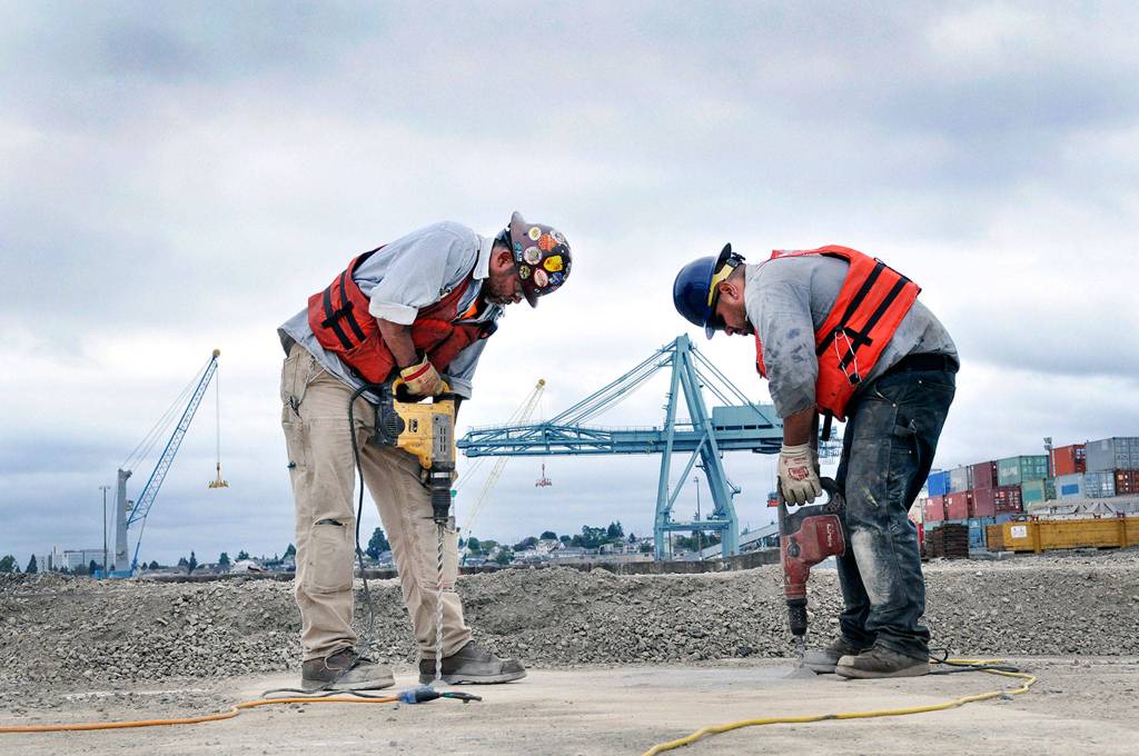 Journeyman pile driver Eugene Bowen (left) and Chris McKinsey, an apprentice pile driver, drill holes for a containment apparatus that will help keep concrete from falling in the water as work is being done on the pier at the Everett waterfront. Read about new development at the port <a href="https://www.heraldnet.com/business/buildings-are-rising-along-the-waterfront-and-on-the-river/" target="_blank">here</a>. (Sue Misao / The Herald)