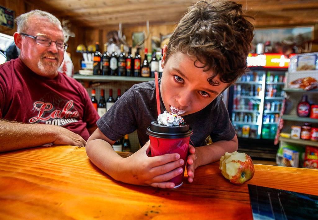 Owner Kevin Hickson says one of the things he has enjoyed most about running the Lake Roesiger Store has been the kids. Here, he visits with Sawyer Hoenshell, 4, who puts aside an apple and devours a hot chocolate with whipped cream and sprinkles. (Dan Bates / The Herald)