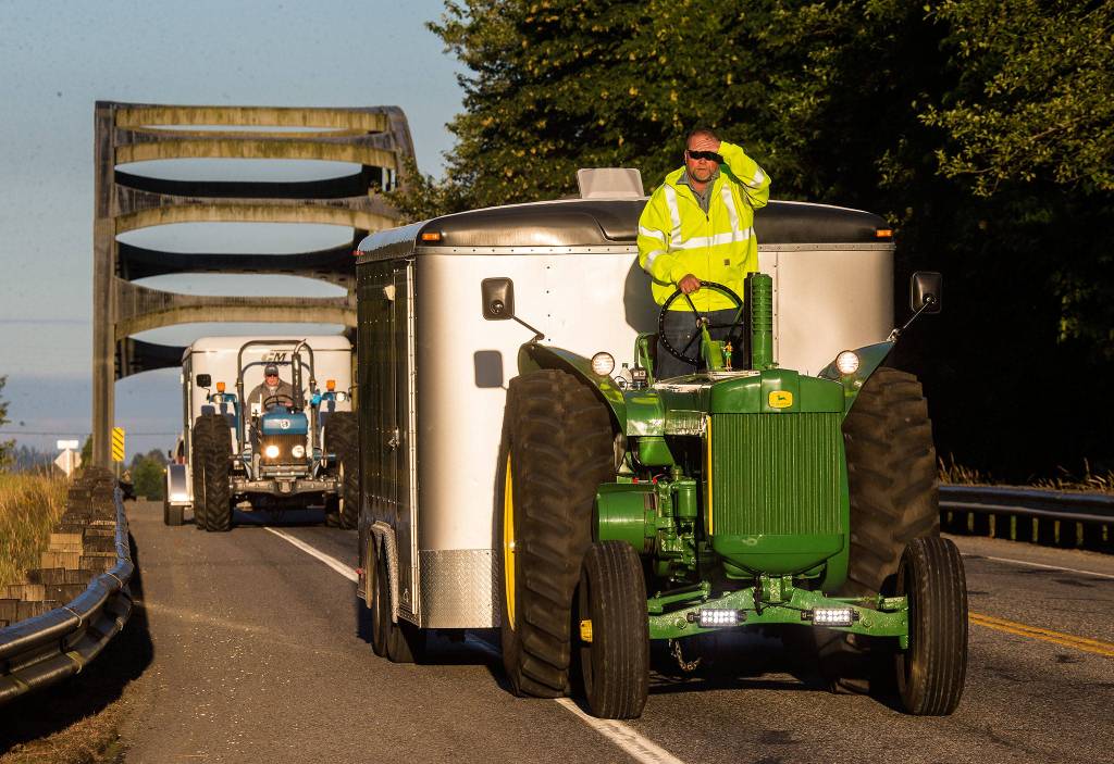 Jeff Newell blocks the early morning sun from his eyes as he cruises down Highway 530, at a easy 16 miles per hour, on his John Deere tractor on July 11 in Arlington. Ron Wachholtz follows behind as the two raise money for the American Diabetes Association while <a href="https://www.heraldnet.com/news/slow-ride-from-arlington-to-alaska-on-a-john-deere-tractor/" target="_blank">driving their tractors to Prudhoe </a><a href="https://www.heraldnet.com/news/slow-ride-from-arlington-to-alaska-on-a-john-deere-tractor/" target="_blank">Bay</a>, Alaska. (Andy Bronson / The Herald)