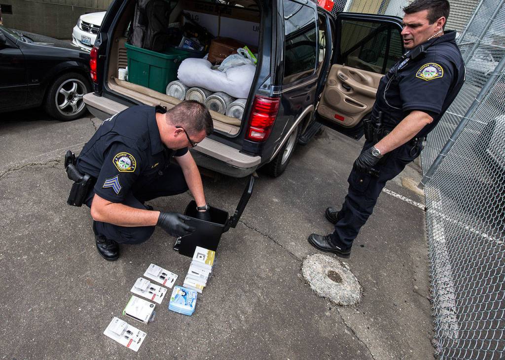 Monroe police Sgt. Paul Ryan pulls electronic items out from a small garbage can during a vehicle search as officer Scott Kornish watches on Thursday, June 14, 2018 in Monroe. (Andy Bronson / The Herald)