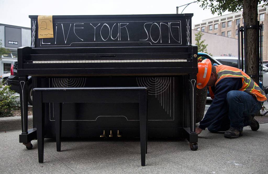 An Everett Public Works employee straps the Live Your Song piano into place in front of Major League Pizza in Everett on Aug. 1. (Olivia Vanni / The Herald)