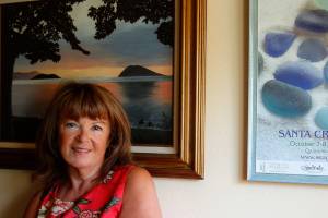 The painting in Linda Smiths den, painted by a family friend in the 70s, is of the beach on Samish Island where Smiths grandmother taught her how to look for things that capture light. The artistic poster (right) from the Sea Glass Festival in Santa Cruz reminds her how she fell in love with Monterey Bay when she first displayed her wares at the event. (Dan Bates / The Herald)