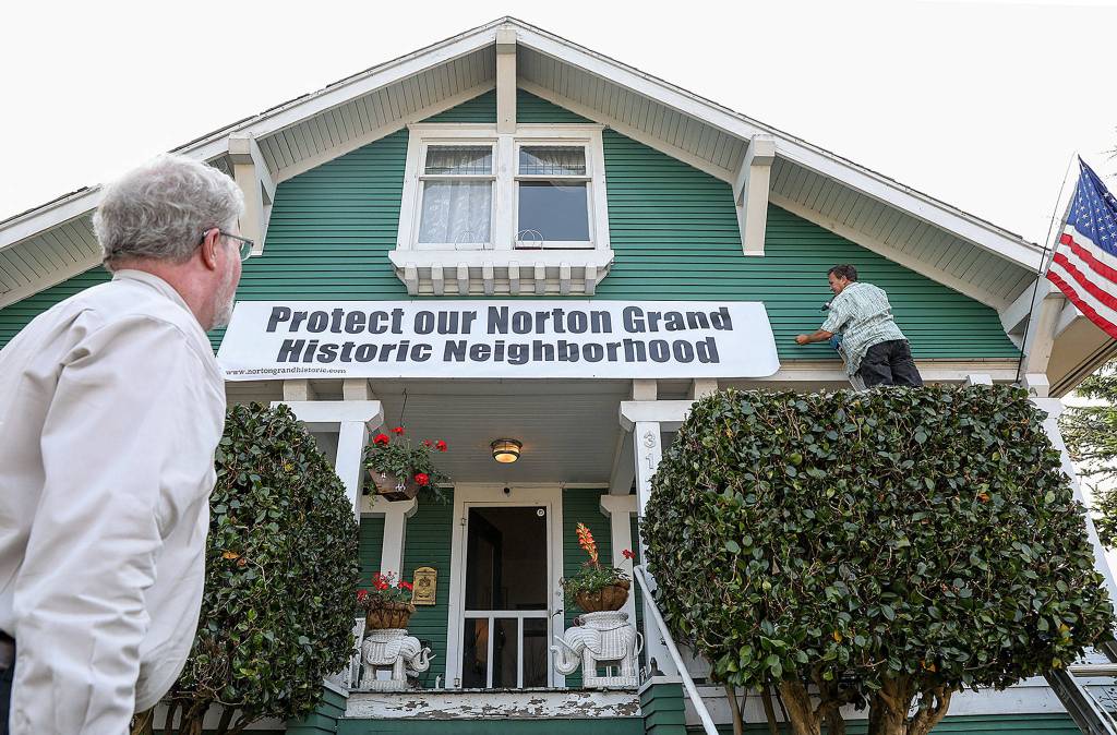 Stuart Cole, right and Jim Dean, both residents of the Grand Norton neighborhood, hang a large banner as the historic district mounts a defense against the Metro Everett plan. (Lizz Giordano / The Herald)