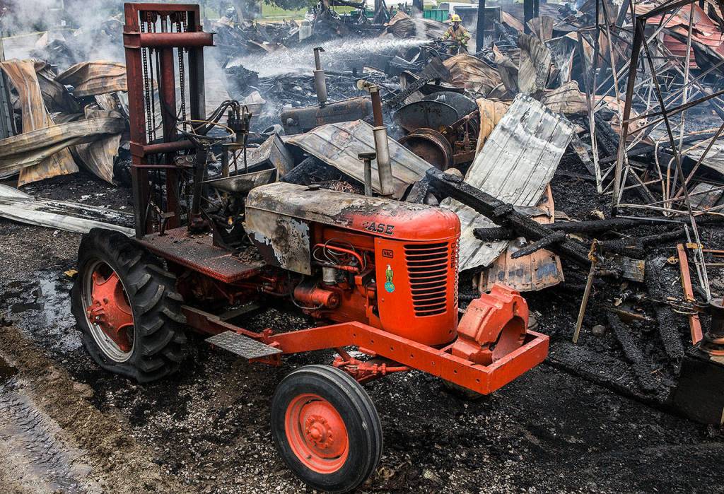 A Monroe firefighter sprays water over the hotspots of the 100-year-old barn that caught fire at the Sky Valley Stock and Antique Tractor Show groundson Aug. 11 in Monroe.(Olivia Vanni / The Herald)