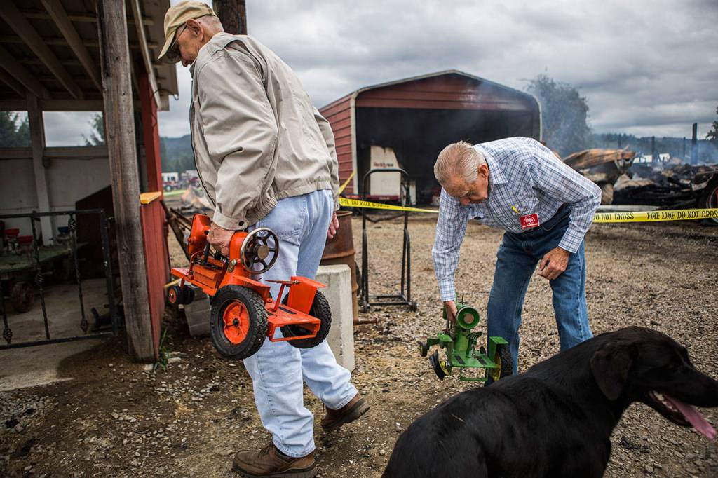 Ernie Odegaard, left, and Bill Wojciechowski carry small model tractors that were salvaged from the barn fire at the Sky Valley Stock and Antique Tractor Show grounds on Aug. 11 in Monroe. (Olivia Vanni / The Herald)