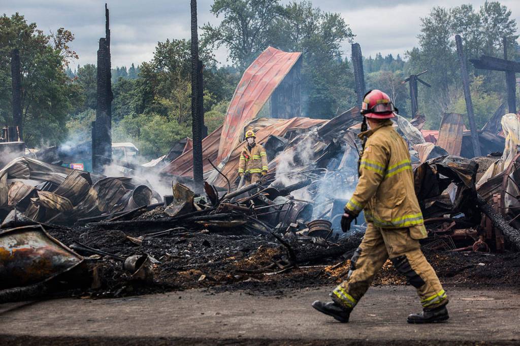 Monroe firefighters walk around the site of the barn fire at the Sky Valley Stock and Antique Tractor Show grounds on Saturday, Aug. 11, in Monroe. (Olivia Vanni / The Herald)