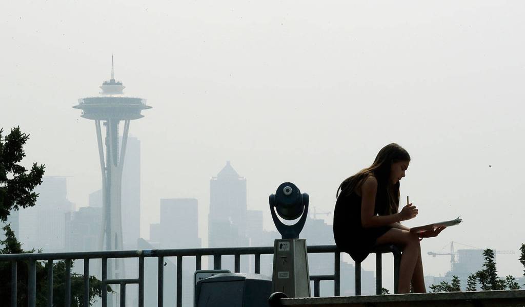A girl works on a drawing next to an unused viewing scope Tuesday as a smoky haze obscures the Space Needle and downtown Seattle behind. Public-health officials are warning of unhealthy air across parts of the Pacific Northwest as smoke from wildfires move across the region. (AP Photo/Elaine Thompson)