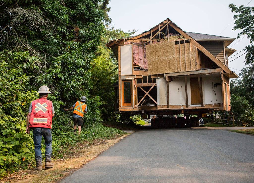 Casjen Cramer, left, and Cody Robertson, of Nickel Bros., watch as the house being moved down Bellflower Road in Bothell on Wednesday just clears a tree. (Olivia Vanni / The Herald)