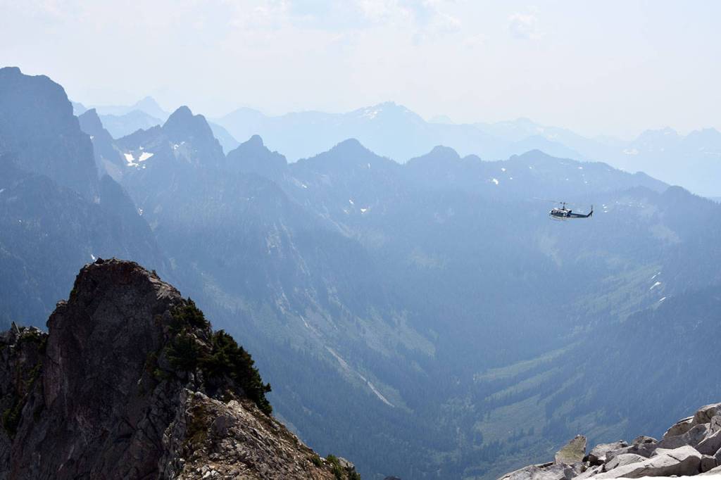 A helicopter soars southeast of Vesper Peak, searching for missing hiker Sam Sayers, 27, of Seattle. The background is a valley at the headwaters of the Sultan River. (Caleb Hutton / The Herald)