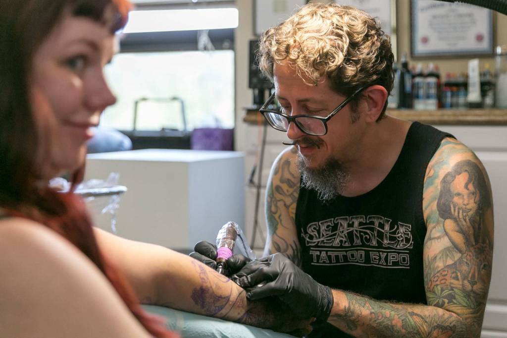 Abigail Espinoza (left) is tattooed by <a href="https://www.heraldnet.com/life/everett-tattooist-has-been-to-every-single-seattle-tattoo-expo/" target="_blank">Michael Gardner of Tattoo Garden</a> at his shop in Lowell on Aug 8, 2018. (Kevin Clark / The Herald)