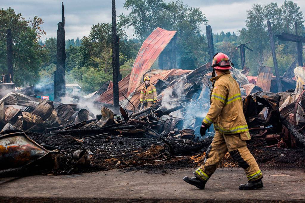Monroe firefighters walk around the site of the <a href="https://www.heraldnet.com/news/fires-cancel-tractor-show-in-monroe-burn-trailer-in-maltby/" target="_blank">barn fire</a> at the Sky Valley Stock and Antique Tractor Show grounds on Aug. 11, 2018 in Monroe. (Olivia Vanni / The Herald)