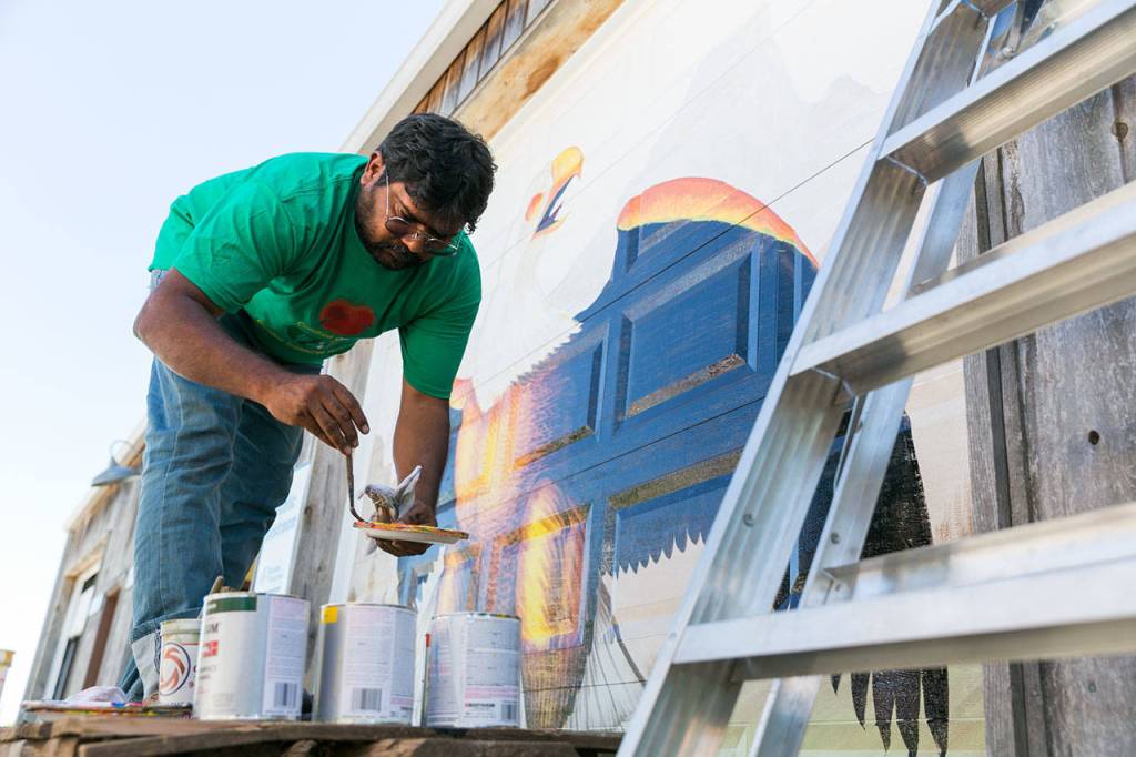 Haider Ali paints the garage doors of Garden Treasures Nursery & Organic Farm in Arlington on Aug. 7. (Kevin Clark / The Herald)