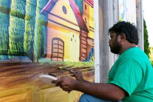 Haider Ali paints the garage doors of Garden Treasures Nursery & Organic Farm in Arlington on Aug. 7. (Kevin Clark / The Herald)