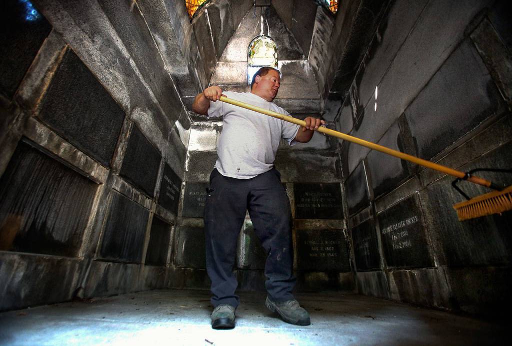 Shane Willis sweeps out the Rucker Tomb after opening it for Bill Rucker. (Dan Bates / The Herald)