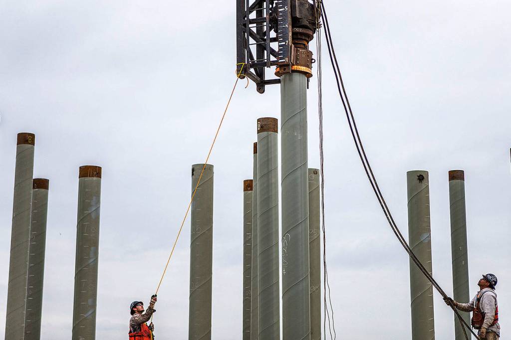 Two workers align the pile driver the pile during construction at the Port of Everett on Aug. 17, 2018 in Everett, Wa. (Olivia Vanni / The Herald)
