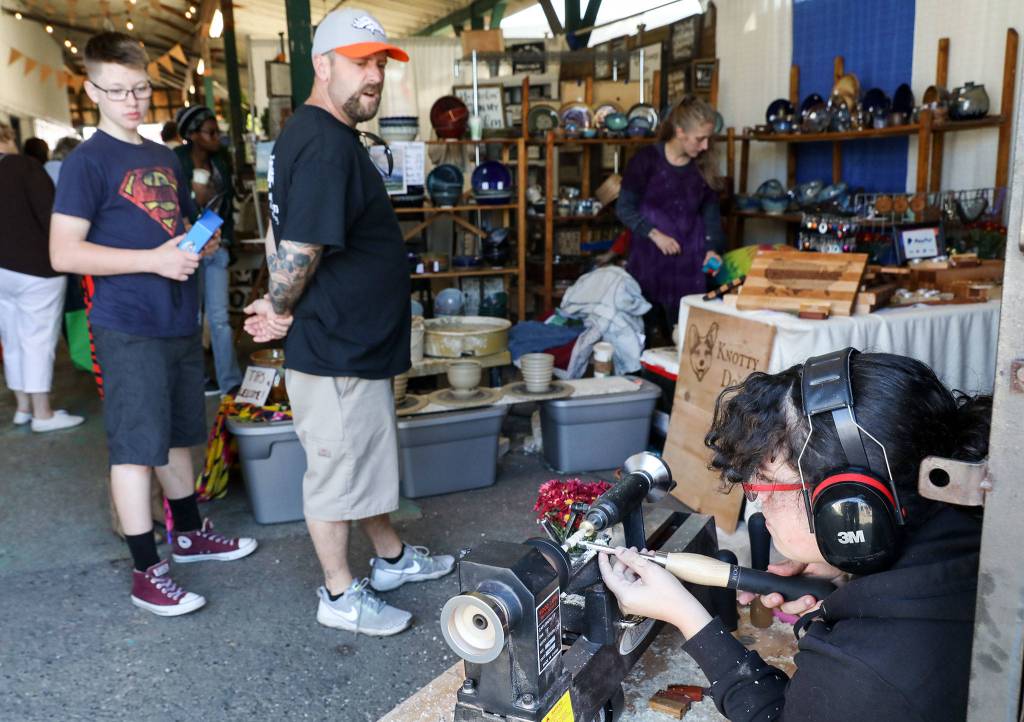 Angela Liberty, who runs Knotty Dog Craftworks with her husband, Stephen, demonstrates how she turns pens by hand on her lathe. (Lizz Giordano / The Herald)