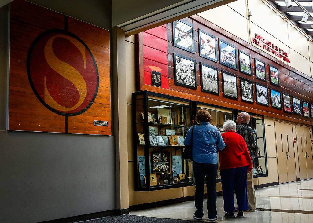 A Snohomish High graduate from the Class of 1942 (center) and others look at trophies and photographs from the schools many state championship teams. (Dan Bates / The Herald)