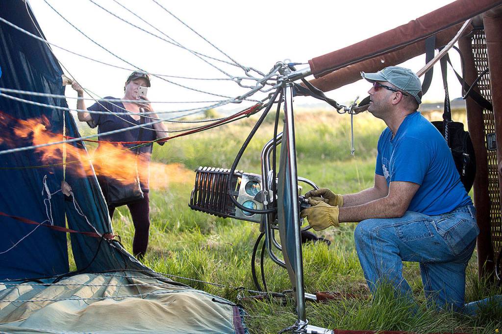Kelly Vice holds open the balloon and takes a cellphone photo as Woodward directs hot air into the balloon. (Andy Bronson / The Herald)