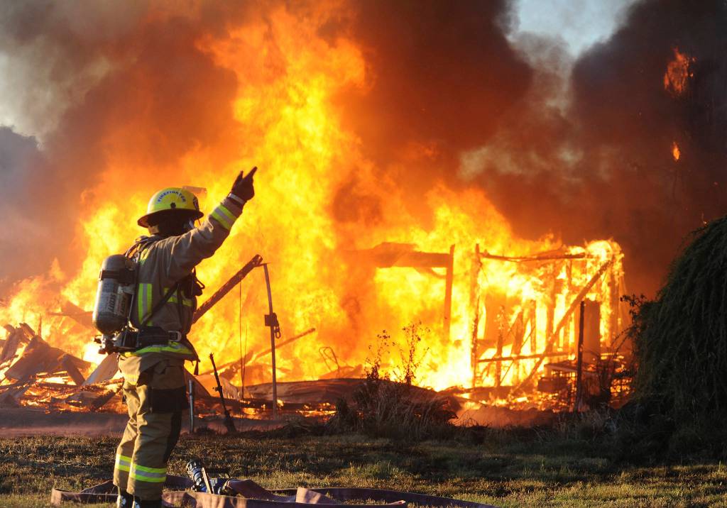 A Snohomish Fire District 4 firefighter signals for water to his hose as he prepares to attack <a href="https://www.heraldnet.com/news/gallery-flames-fill-the-sky-near-snohomish/" target="_blank">a fire</a> that destroyed an out building on the Fobes Road, west of Snohomish, on Sept. 17. (Doug Ramsay / For the Herald)