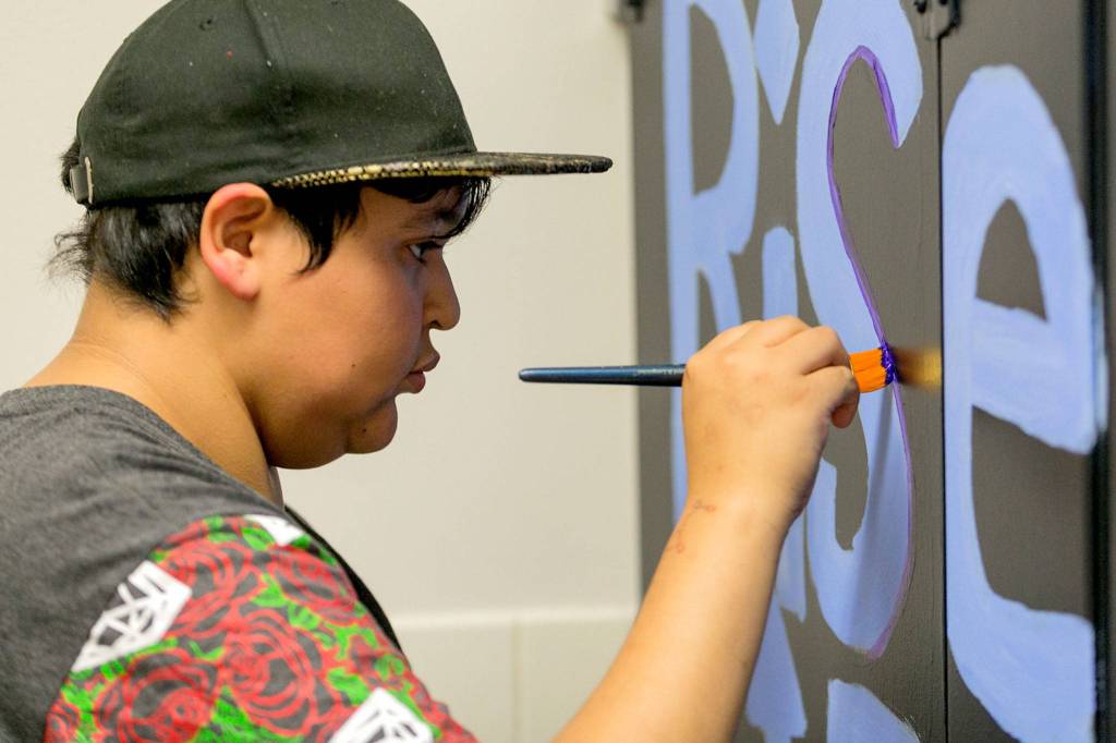 Alejandro Ramos paints the stall door in the mens room at Crossroads High School in Granite Falls on Sept. 11. (Kevin Clark / The Herald)