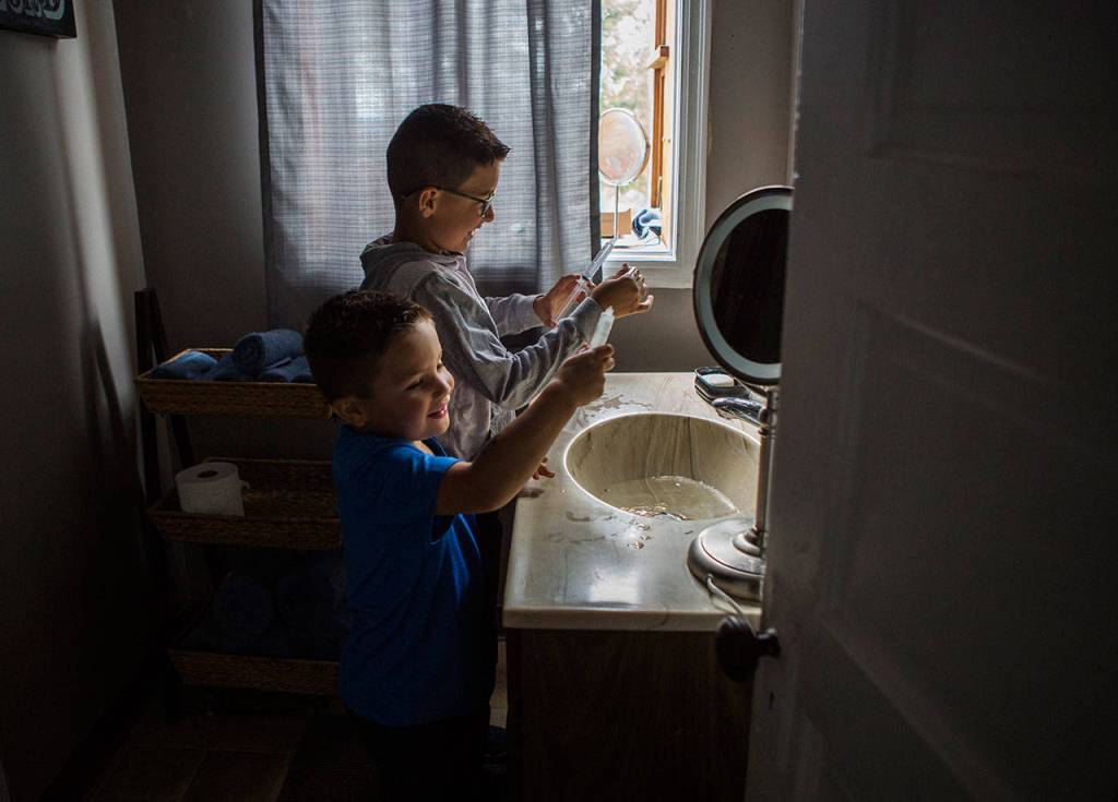 Samuel Avalos, 4, and brother Timothy Avalos, 7, fill Samuels empty syringes with water to spray at their sister at their familys home Aug. 30 in Snohomish. (Olivia Vanni / The Herald)