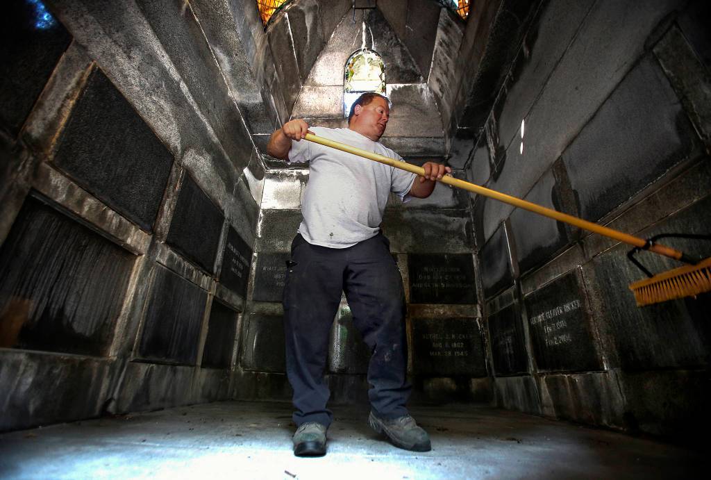 Shane Willis sweeps out the Rucker Tomb after opening it for Bill Rucker. (Dan Bates / The Herald)