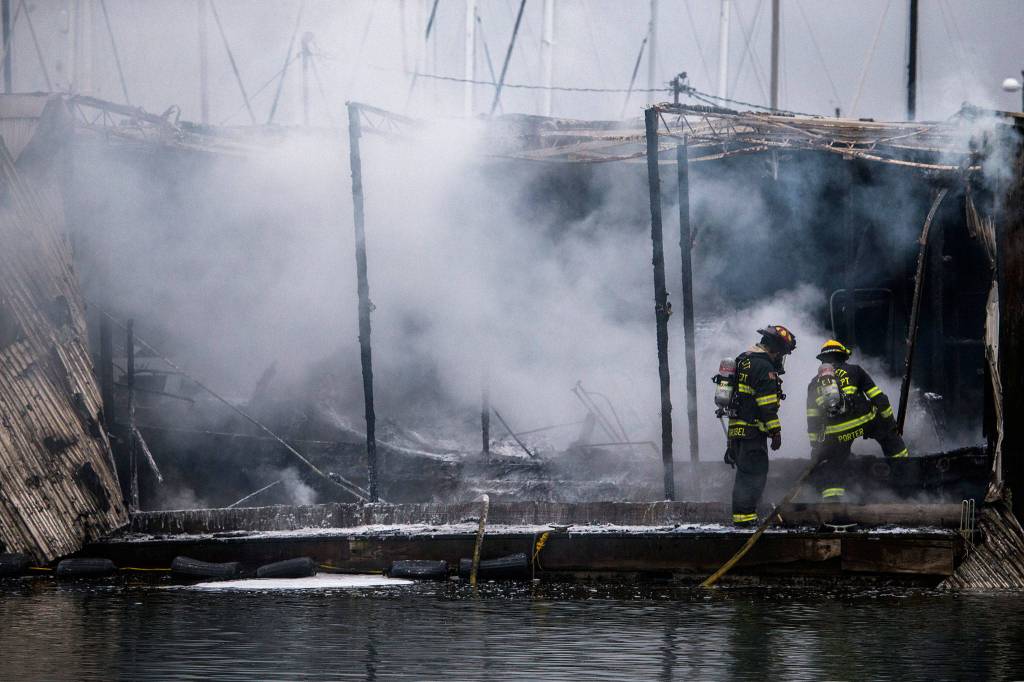 Everett firefighters step on to what is left of a boat that burned in a fire Oct. 8, at the Port of Everett marina. (Olivia Vanni / The Herald)