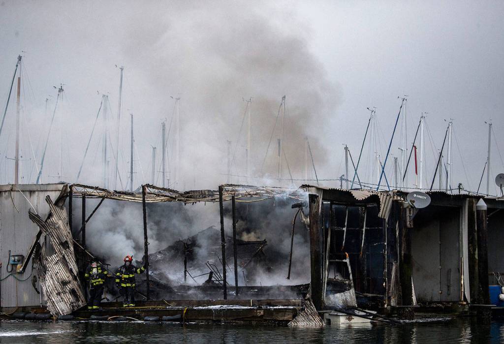 Firefighters stand on a dock next to a boat that burned in a fire Oct. 8, at the Port of Everett marina. (Olivia Vanni / The Herald)