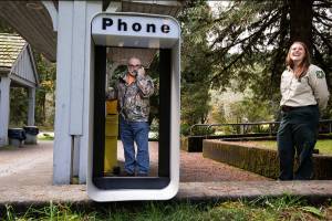 Verlot Corridor Manager Erica Keene laughs as Richard Bake, tech support for Snohomish County, talks to a 911 operator after installing the new pay phone at the Verlot Public Service Center on Tuesday, Oct. 9, 2018 in Verlot, Wa. The installation by Snohomish County puts a permanent payphone in the town of Verlot, a valuable public safety asset in an area with little cellphone service. (Andy Bronson / The Herald)