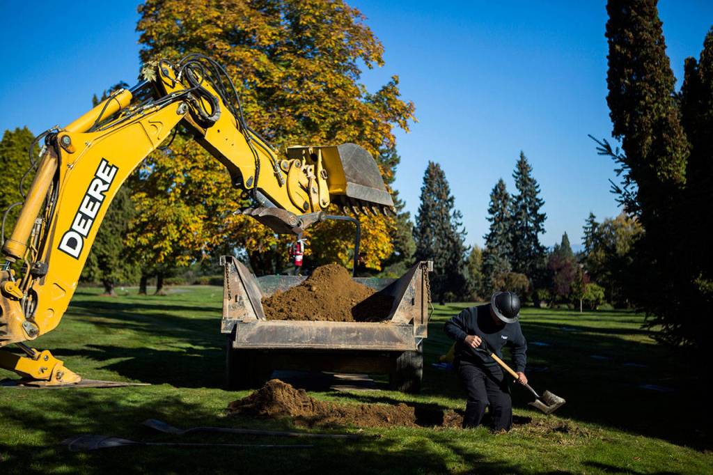 A worker helps shovel dirt from the John Doe grave at Cypress Lawn cemetery on Oct. 17 in Everett. (Olivia Vanni / The Herald)