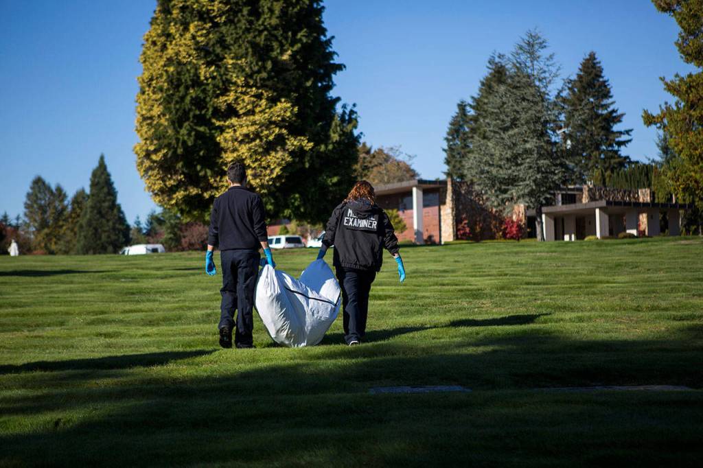 Two employees with the Snohomish County Medical Examiners Office help carry remains of a John Doe to their van at Cypress Lawn cemetery on Oct. 17 in Everett. (Olivia Vanni / The Herald)