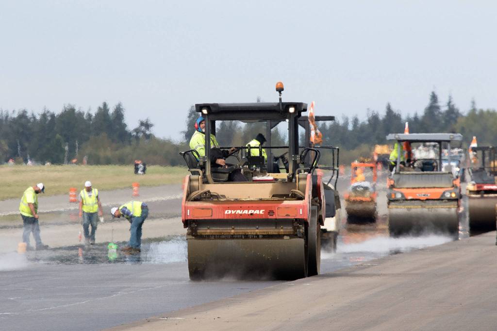 One of nearly a dozen steamroller operators reverses down the runway at Paine Field while workers check compaction of the new asphalt on Oct. 3 in Everett. (Andy Bronson / The Herald)