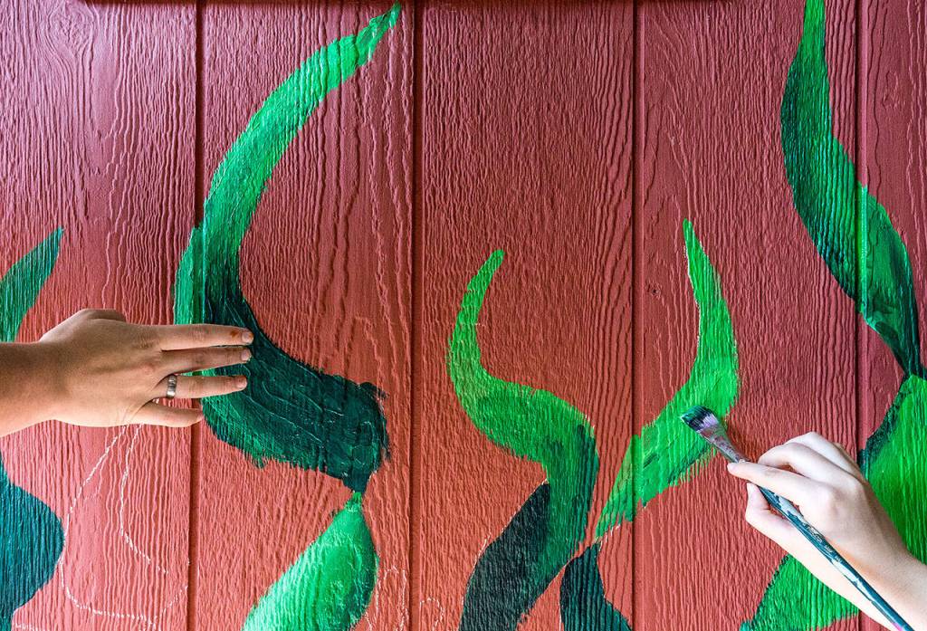 Snohomish High School students blend colors using finger and brush to create seaweed a tiny home Monday in Snohomish. (Andy Bronson / The Herald)