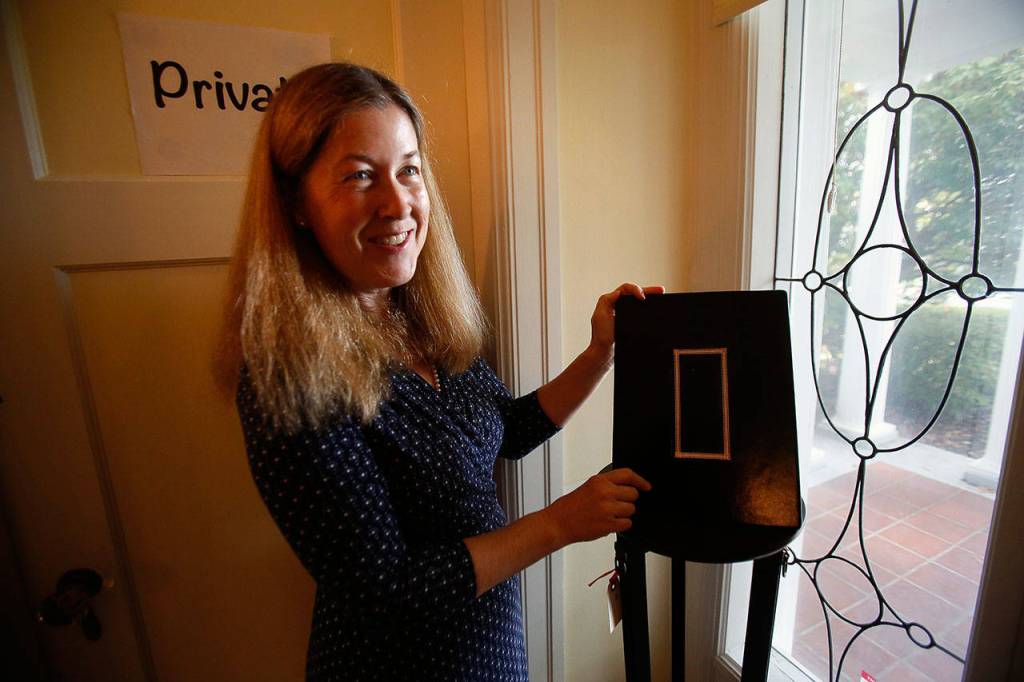 Anna Marie explains one of many unusual pieces around the Jackson house. This one, stationed near the main entrance, is created to easily display guest seating arrangements around the dining room table, which is marked by gold and mounted on dark brown leather. (Dan Bates / The Herald)