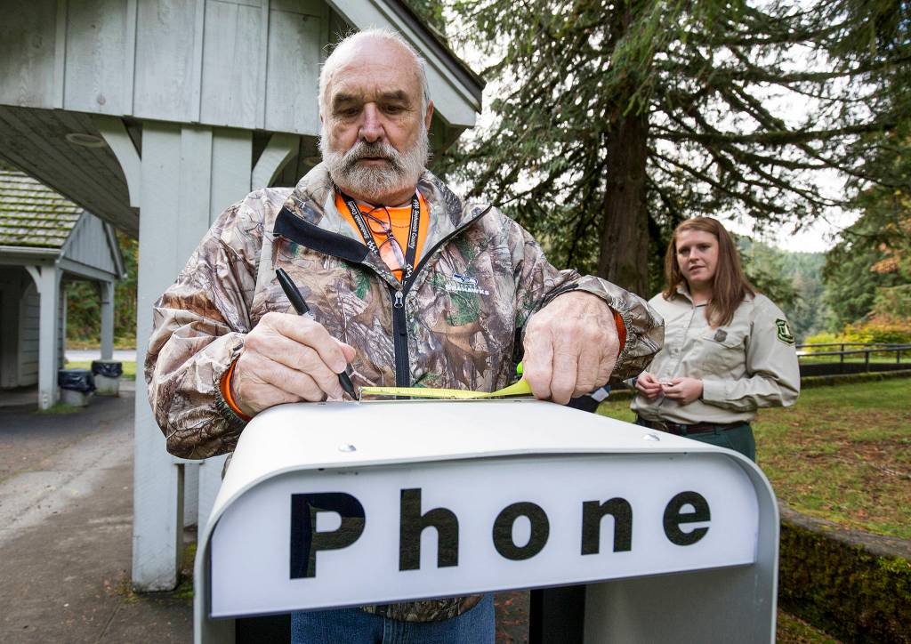 Richard Bake measures the cover case for the new pay phone at the Verlot Public Service Center on Oct. 9 in Verlot. Verlot Corridor Manager Erica Keene watches the installation by Snohomish County. (Andy Bronson / The Herald)
