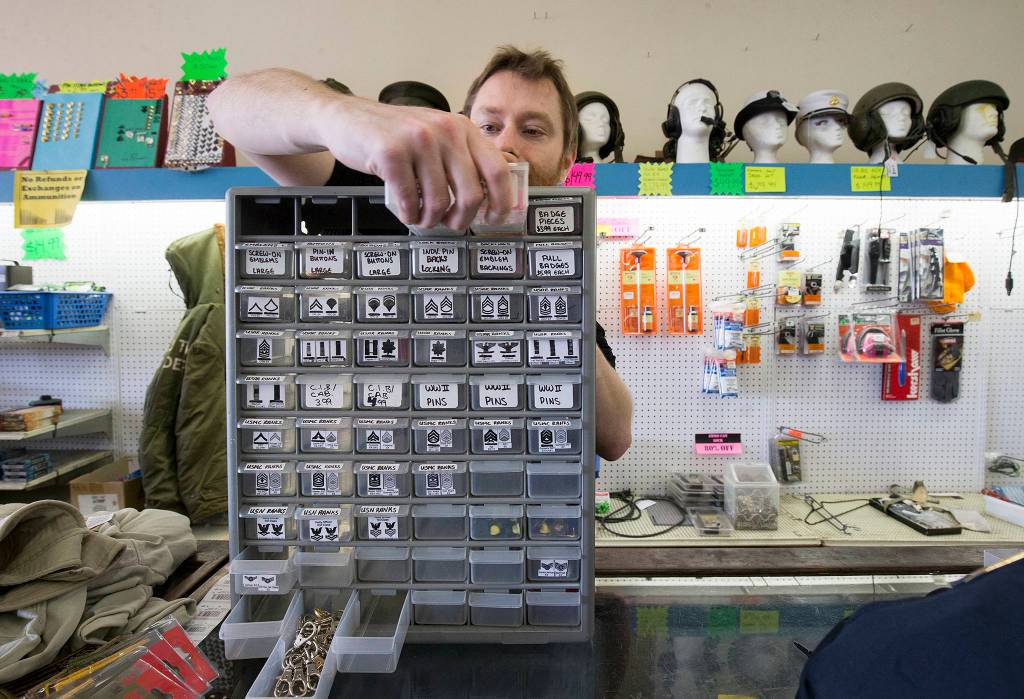 Shawn Winters, grandson of owners Jerry and Donna Winters, pulls out drawers of uniform insignias for a customer at Eds Surplus & Marine on Oct. 10 in Everett. (Andy Bronson / The Herald)