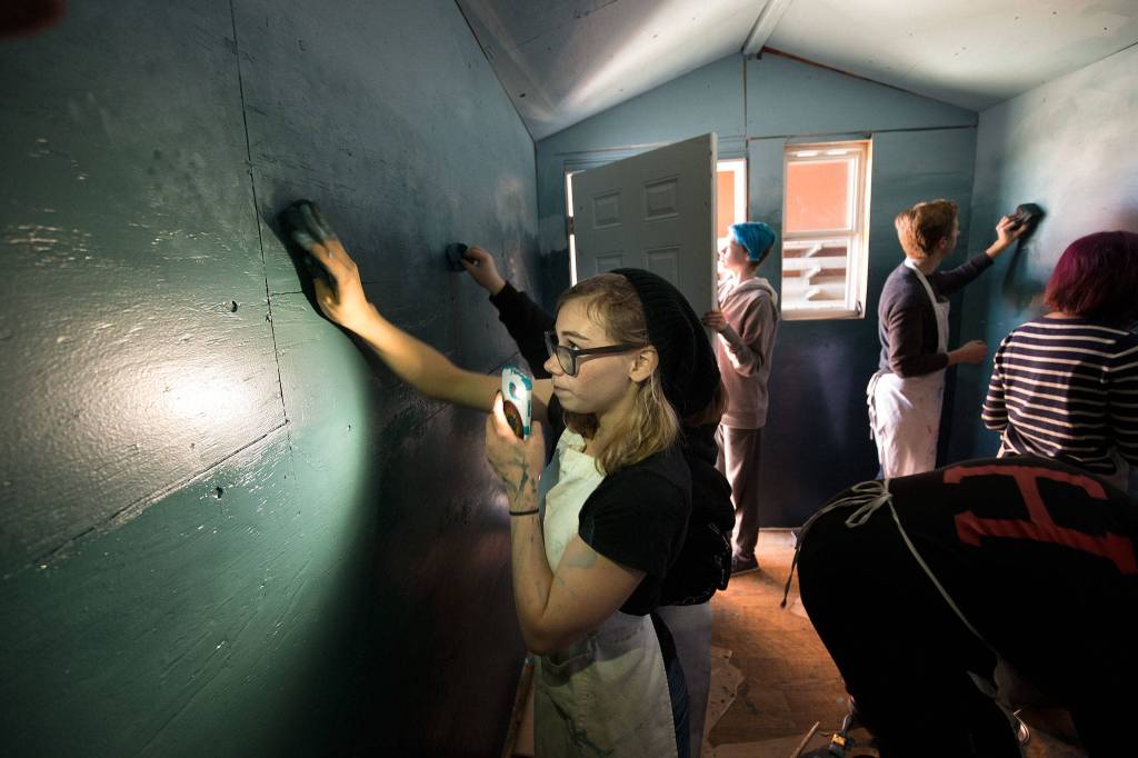 Snohomish High School student Hailey Knie uses her cellphone to light up the wall where she is blending colors of paint in a tiny home at the school on Oct. 22 in Snohomish. (Andy Bronson / The Herald)