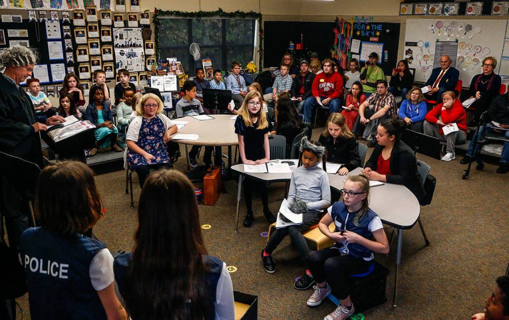 Like a veteran attorney, fifth-grader Runa Lockhart (center) leans forward on her hands and questions fifth-grade police officers Brooke McDugle (left forground) and Leila Andoloro on the witness stand testifying why they arrested Sneezy the Wolf. With furry head and paws, sitting foreground guarded by Sheriff Kaleigh Stull, Sophie McDonald looks like a worried wolf. (Dan Bates / The Herald)